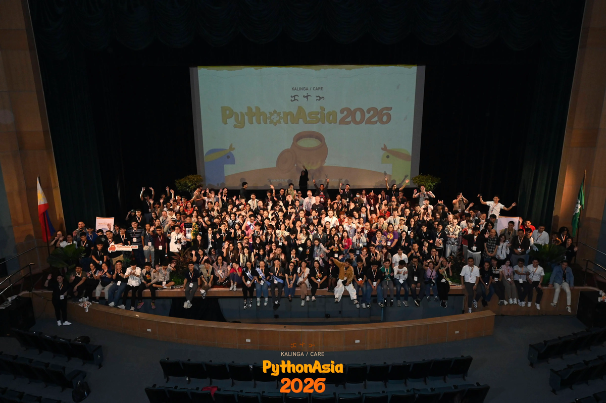 Group photo of community members at a conference on a stage with a screen reading "PythonAsia 2026".