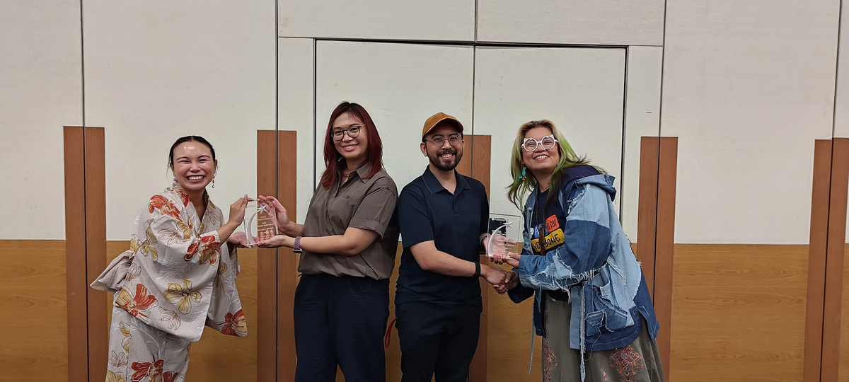 Photograph of Matt and Micaela with Cheuk and Georgi holding the PSF CSA award trophy during an informal celebration event in a bright room.