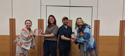 Photograph of Matt and Micaela with Cheuk and Georgi holding the PSF CSA award trophy during an informal celebration event in a bright room.